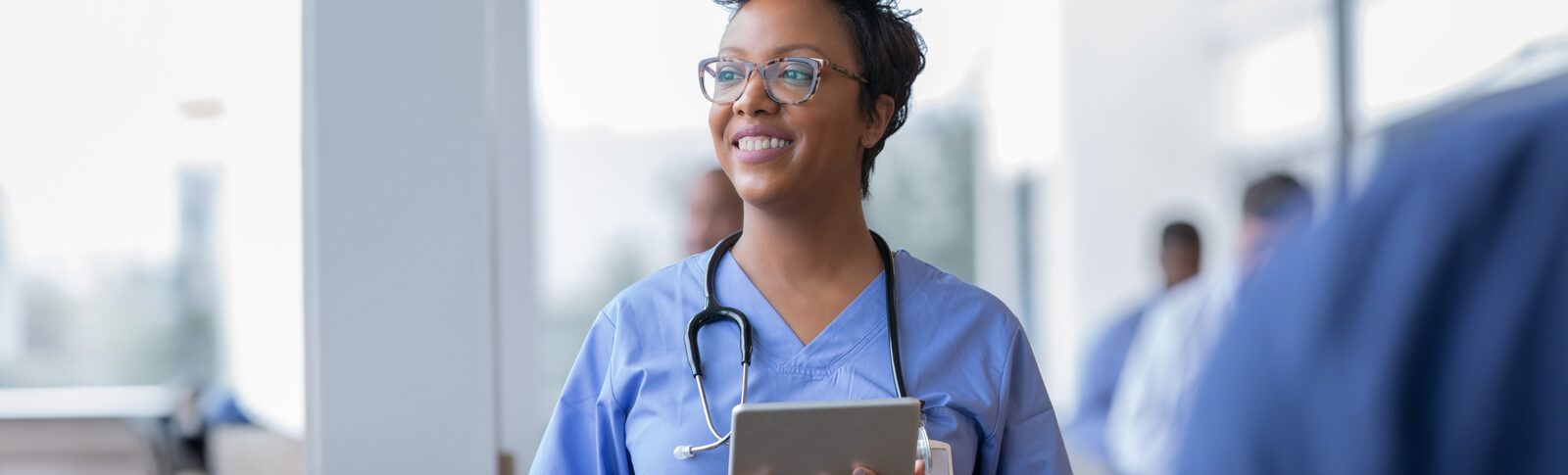 Nurse in blue scrubs smiling while holding a tablet