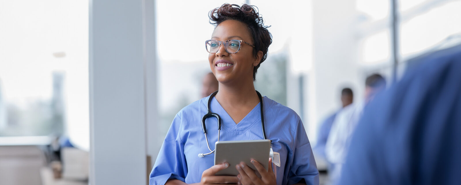 Nurse in blue scrubs smiling while holding a tablet
