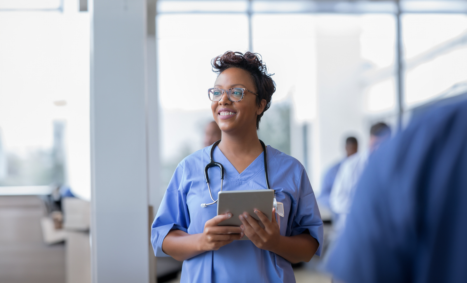 Nurse in blue scrubs smiling while holding a tablet