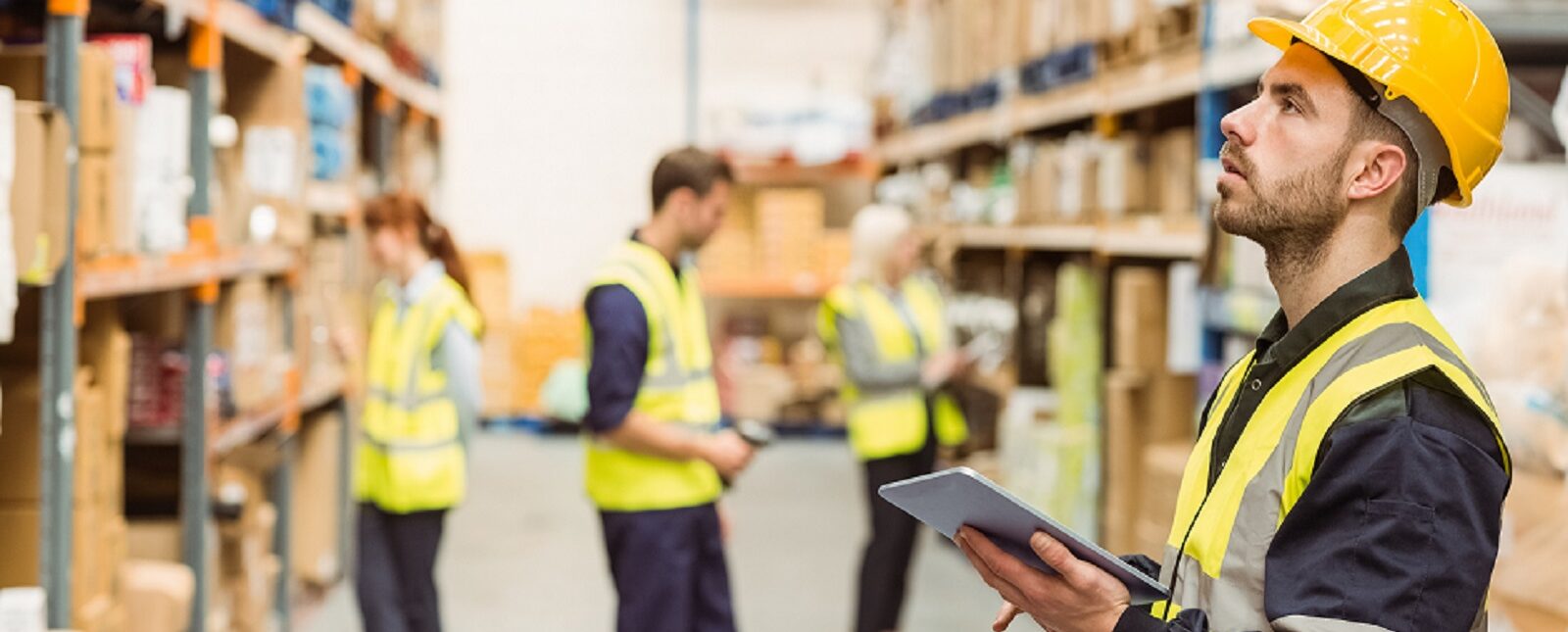 A man in a hard hat and safety vest surveys the warehouse, ensuring safety and compliance in the work area.